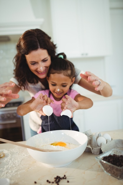 Mother and daughter breaking egg in bowl while preparing cookie