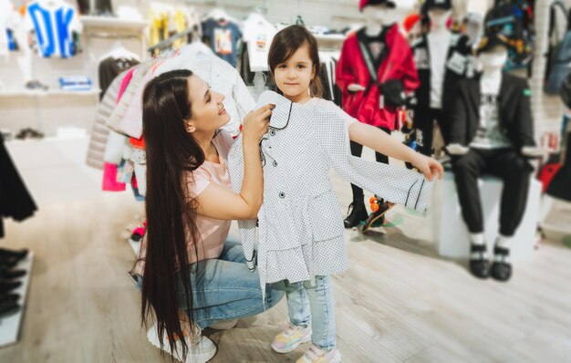 Foto madre e figlia comprano vestiti madre e bambina che provano i vestiti nel negozio