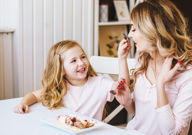 Mother and daughter in a cafe sitting at a table and feed each other ice cream