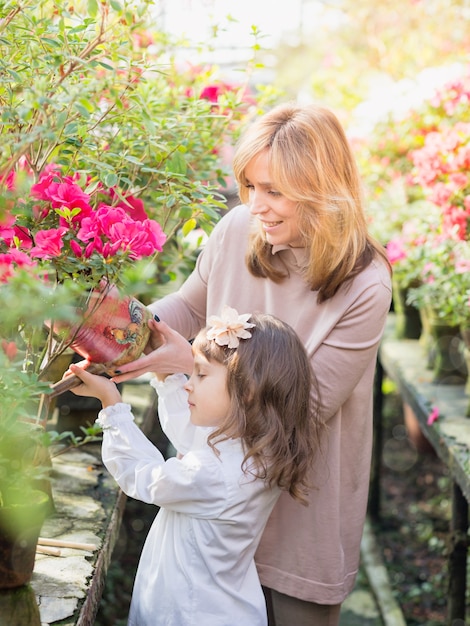 Mother And Daughter carrying plants, gardening In greenhouse.