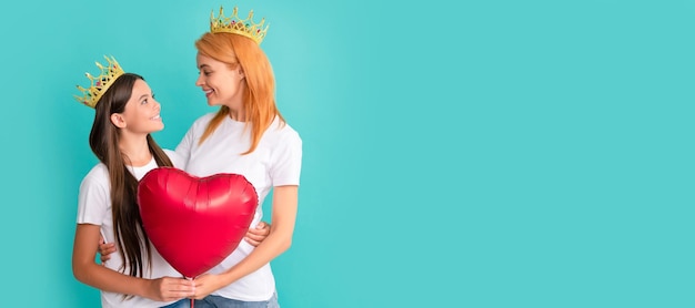 Mother and daughter child banner copy space isolated background Happy woman and girl child in crowns smile at each other holding heart balloon Valentines day
