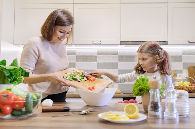 Мать и дочь вместе готовить в кухне овощной салат