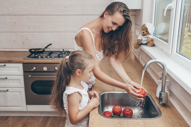 Mother and daughter cooking and washing vegetables in kitchen