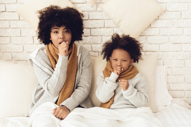 Mother and daughter coughing sitting on bed at home.