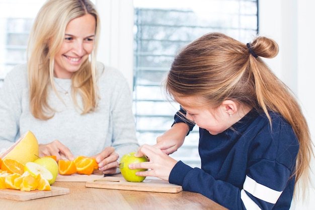 Foto madre e figlia che tagliano frutta sulla tavola a casa