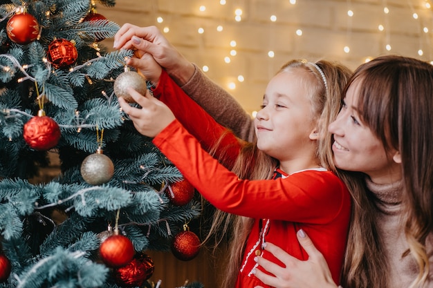 母と娘が一緒にクリスマスツリーを飾ります。伝統的な子育て。