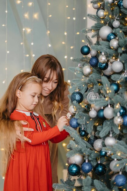 Mother and daughter decorate the Christmas tree together. Traditional parenting.