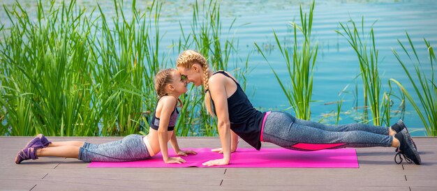 Mother and daughter doing sports exercises on the pier near the water outdoor