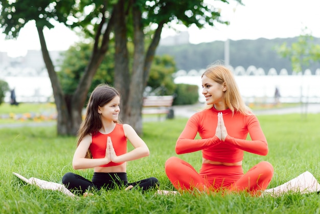 Mother and daughter doing yoga exercises on grass in the park at the day time