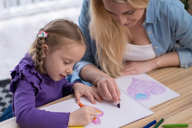 紙にハートの形を描いて着色する母と娘 お母さんが女の子がペイントを学ぶのを手伝う