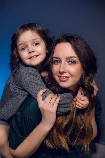 Mother and daughter in dresses sitting on a bed in a bedroom with a blue wall