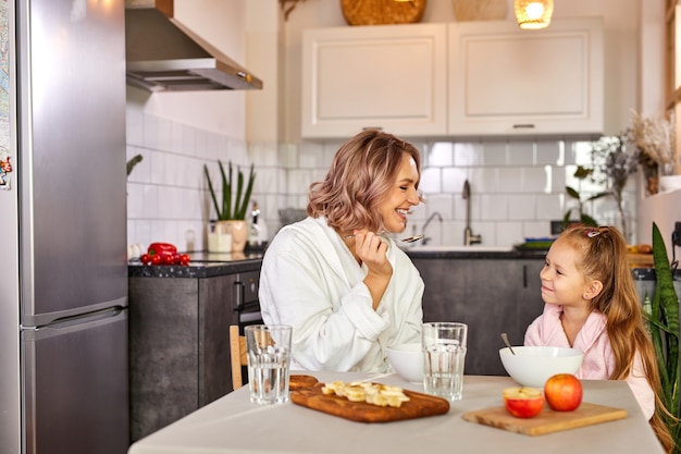 Mother and daughter eating fruit and porridge. healthy nutrition for children, morning meal.caucasian family having breakfast in a light modern kitchen