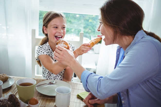 Mother and daughter feeding croissant to each other while having breakfast