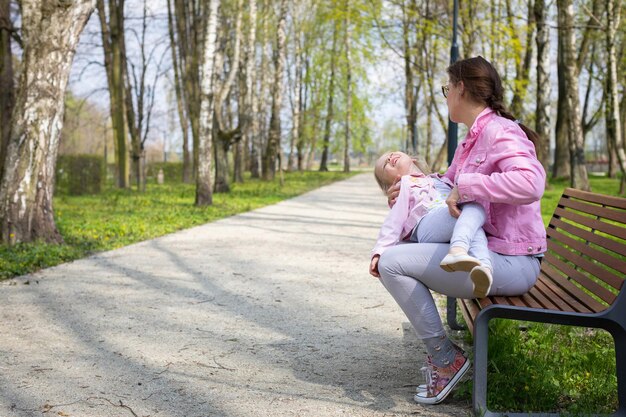 Mother and daughter fooling around while sitting on a bench in a city park