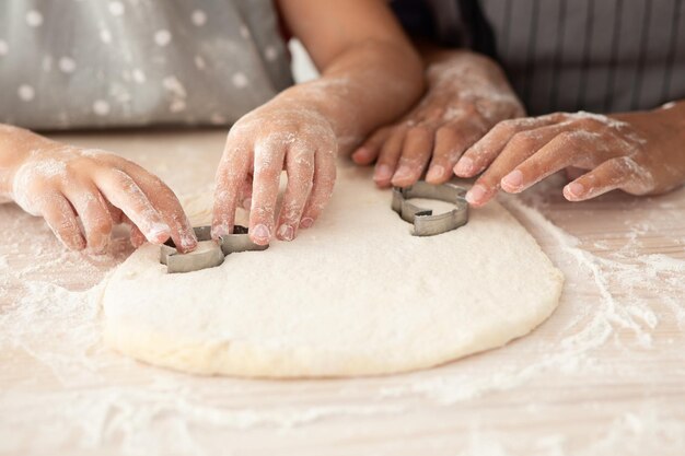 Mother and daughter hands cutting out different cookie shapes\
of dough closeup