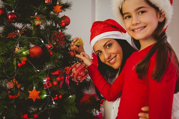 Photo mother and daughter hanging christmas decorations on tree