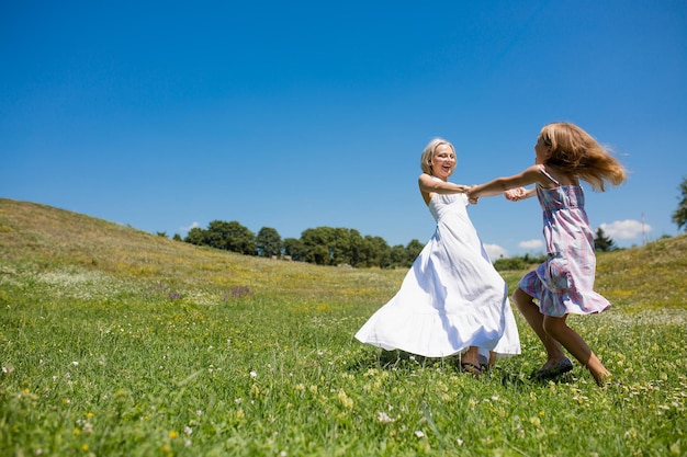 Mother and daughter happlly spinning holding hands. Family love concept, mom in white dress dancing with her girl child.