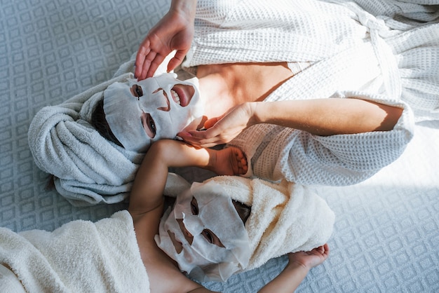 Mother and daughter have spa day with beauty masks on faces. Lying down on bed with towels on heads.