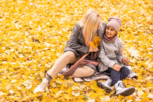 Mother and daughter having fun in the autumn park among the falling leaves.