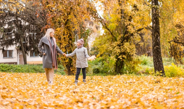 Mother and daughter having fun in the autumn park among the falling leaves.