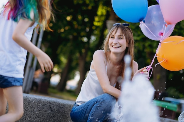 Mother and daughter having fun on girl birthday splashing near city fountain