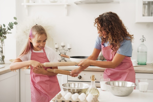 Мать и дочь веселятся со скалкой на кухне во время готовки