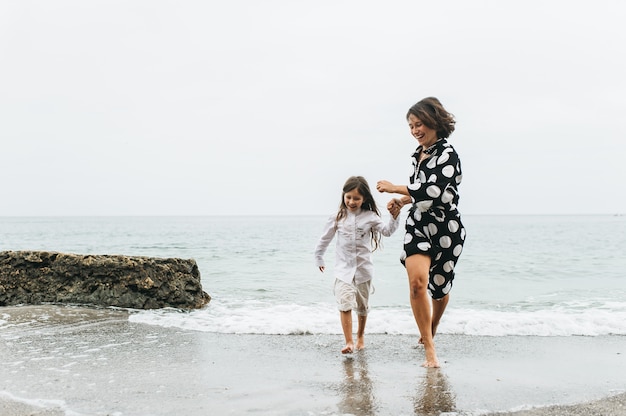 母親と娘が手をつかんでビーチで歩く