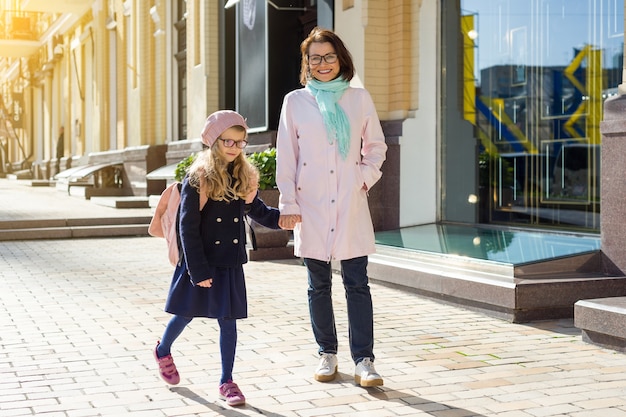 Mother and daughter holds hands, taking together to school