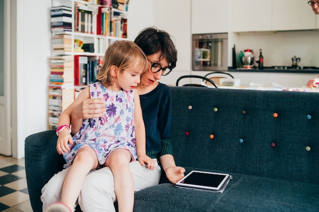 Mother and daughter indoor using tablet sitting couch â learning, entertainment, teaching concept