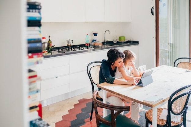 Mother and daughter indoor using tablet sitting table