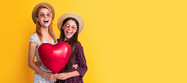 Mother and daughter kid banner copy space isolated background amazed mother and daughter holding love heart balloon on yellow background