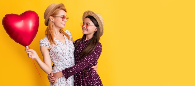 Mother and daughter kid banner copy space isolated background smiling mother and daughter hold love heart balloon on yellow background