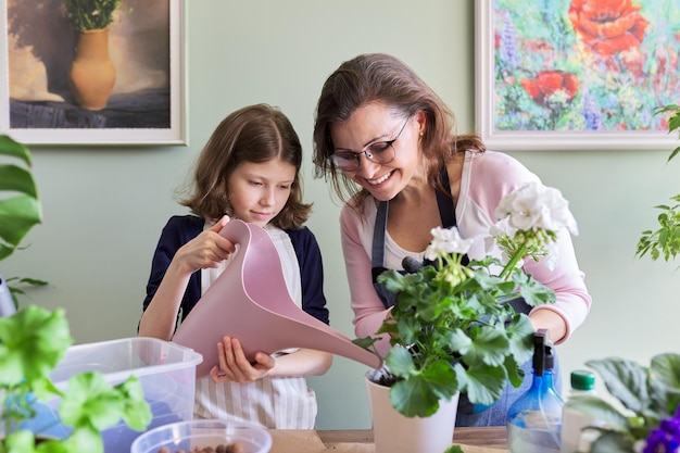 母と娘の子供は一緒に鉢植えの屋内植物の世話をし、女の子はじょうろから花に水をまきます。趣味とレジャー、ケア、家族、観葉植物、ホーム鉢植えの友達のコンセプト