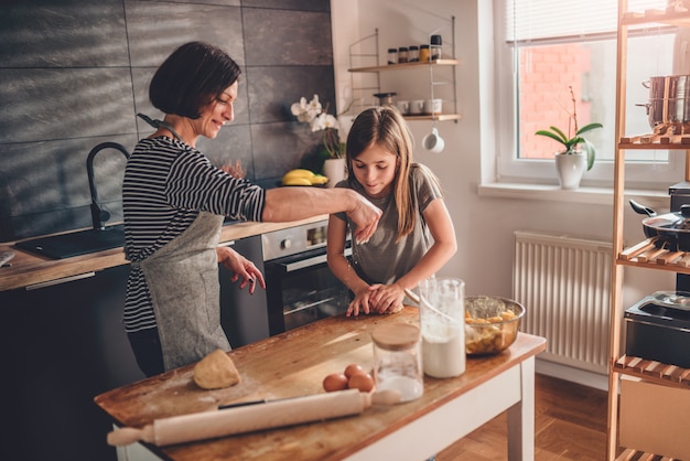 Mother and daughter kneading dough on the wooden table