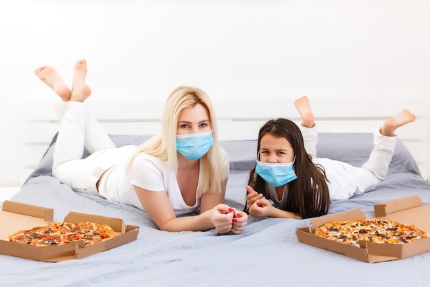 mother and daughter lie in bed at home with pizza during quarantine, quarantine leisure