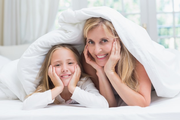 Mother and daughter looking at camera under the duvet 