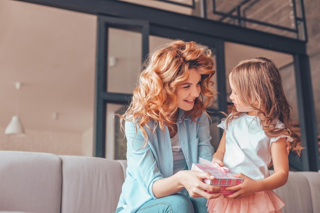 Mother and daughter looking at each other and holding present box at home