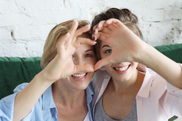 Amore di madre e figlia donna adulta e giovane donna che impilano le mani nel segno del cuore guardando la fotocamera