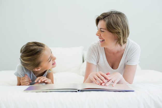 Mother and daughter lying on bed and reading book in bedroom at home