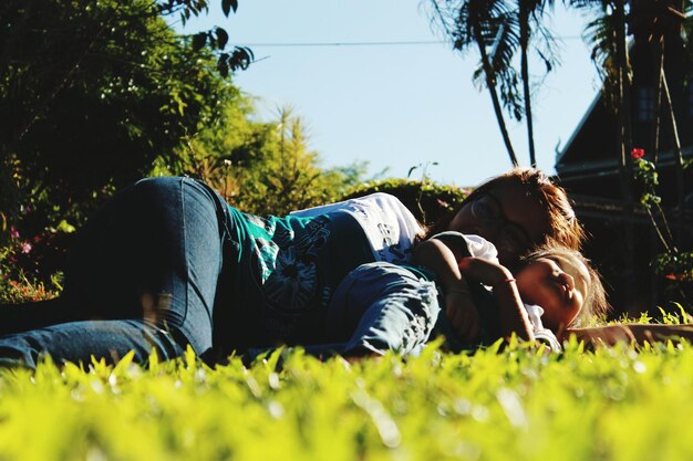 Photo mother and daughter lying down on field against trees