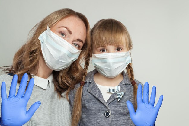 Mother and daughter in medical protective face mask showing stop gesture on white background Covid19 safety concept