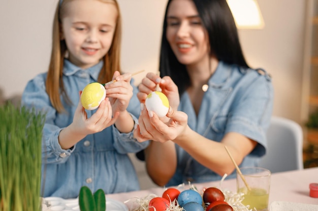 Mother and daughter in modern light kitchen and paining Easter eggs together