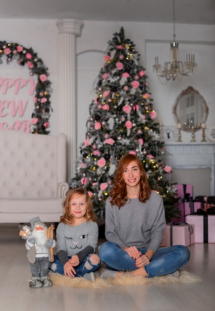 The mother and daughter near Christmas tree sitting on the floor