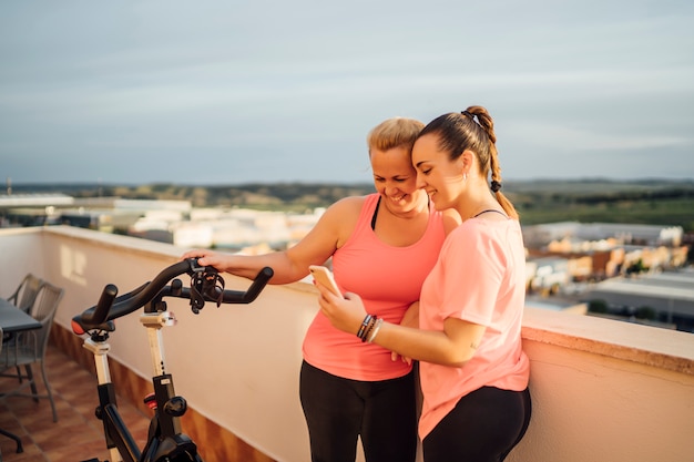 Foto la madre e la figlia eseguono gli esercizi relativi alla ginnastica sul terrazzo domestico facendo uso del telefono cellulare