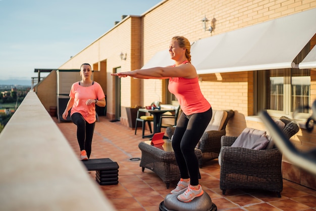 Mother and daughter perform gymnastic exercises on home terrace