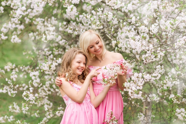 Mother and daughter in pink dresses in a blooming garden in spring.