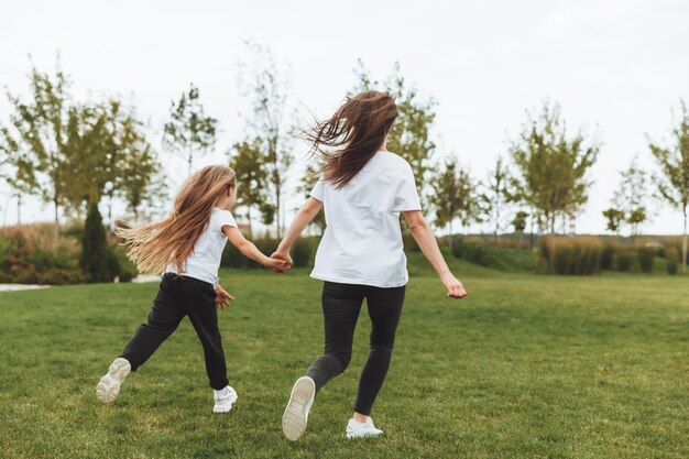 Photo mother and daughter play and run around the park on a beautiful day the family is having fun in the park on the grass morning jog