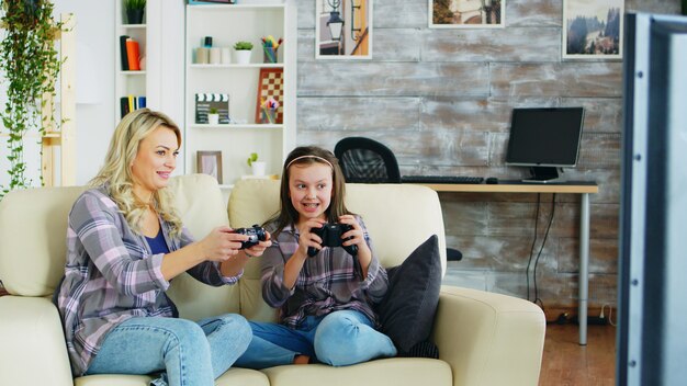 Mother and daughter playing video games using wireless controller sitting on the couch.