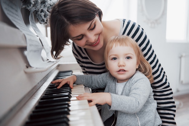 Mother and daughter playing white piano, close up wiew