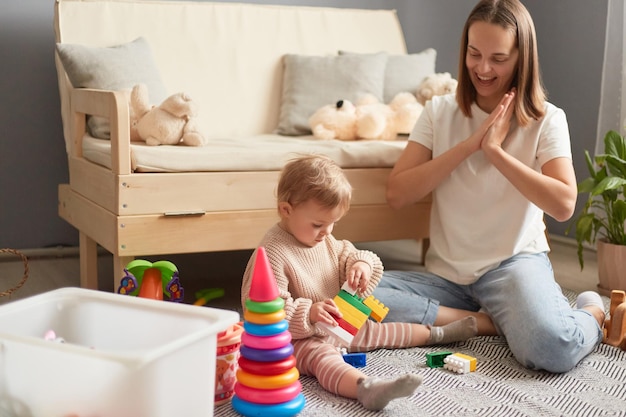 Mother and daughter playing with colorful blocks on the floor of the living room at home Activities with children inside early childhood development